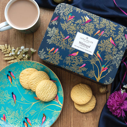 Tea and biscuit selection tin with Smokey Birds design on a table, with mug of tea and plate with shortbreads.