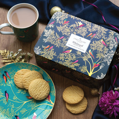 Tea and biscuit selection tin with Smokey Birds design on a table, with mug of tea and plate with shortbreads.