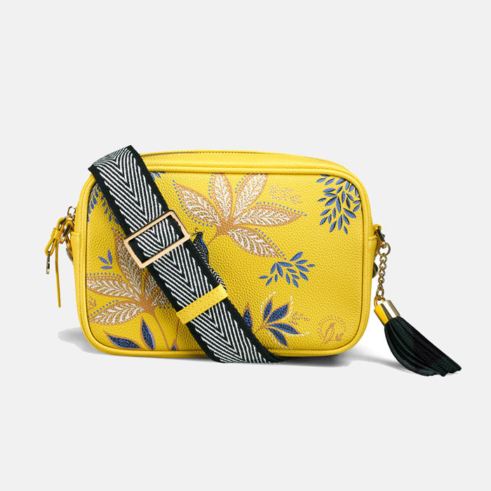 Yellow crossbody handbag with floral design and black tassel, shows back and white chevron strap.