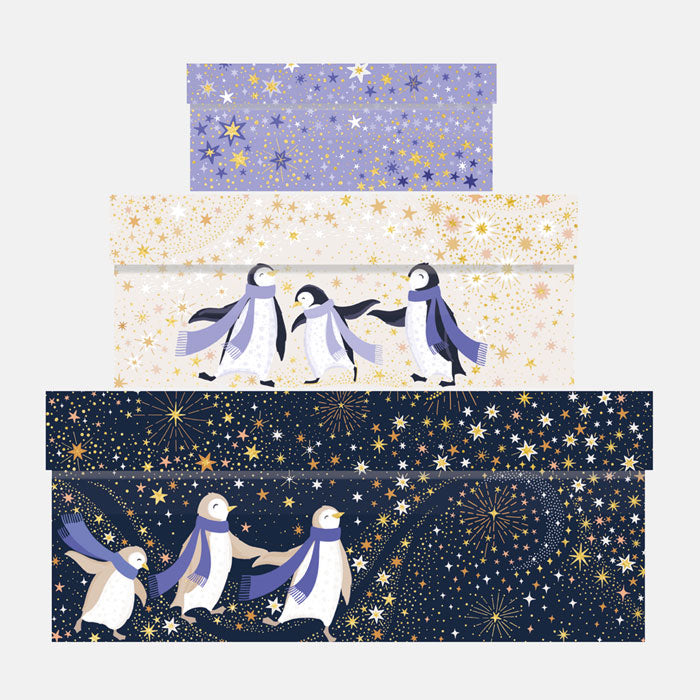 Three stacked rectangular gift boxes with winter-themed designs, with penguins wearing blue scarves against blue and cream starry backgrounds.