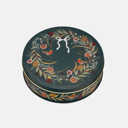A round decorative tin with a dark green lid featuring a hand-painted wreath of leaves, berries, small birds, and citrus slices, accented with a white bow motif at the top center.