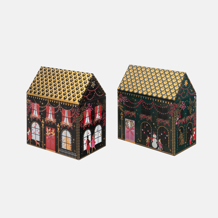 Two small decorative house-shaped tins with festive illustrations. One tin shows a festive red and gold front with windows and holiday figures, and the other shows a dark green front with garlands, lights, and a snowman.