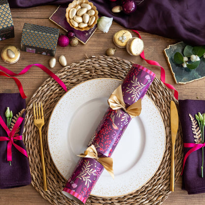 Plum Christmas cracker decorated with pink foliage pattern set on a table place setting.