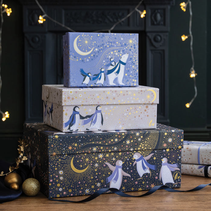 A stack of three gift boxes in a set, all with polar bears and penguins under starry skies and crescent moons. In navy, periwinkle and cream colours with gold embellishment. 