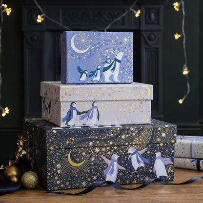 A stack of three gift boxes in a set, all with polar bears and penguins under starry skies and crescent moons. In navy, periwinkle and cream colours with gold embellishment. 
