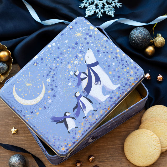 A periwinkle rectangular tin with a polar bear and penguins dressed in purple scarves under a starry sky and crescent moon with gold embellishment.