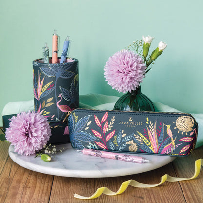 Pencil case with floral design on blue background on a marble tray with flowers and pens, against a light green backdrop.