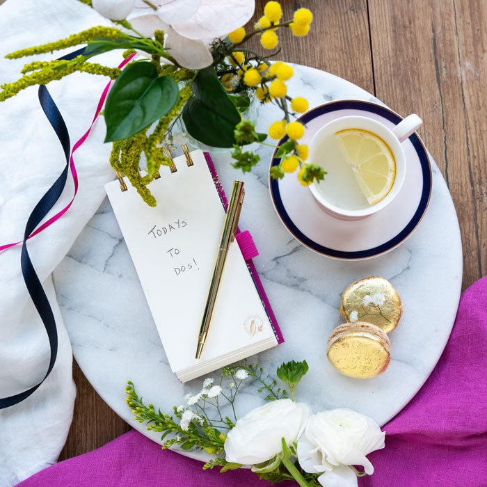 Notepad and pen set on a marble tray with flowers, shows blank pages.