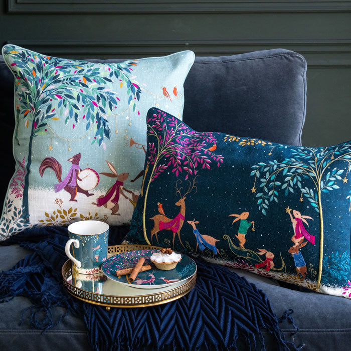 Decorative pillows with festive designs on a sofa with a small table holding a mug and snacks.