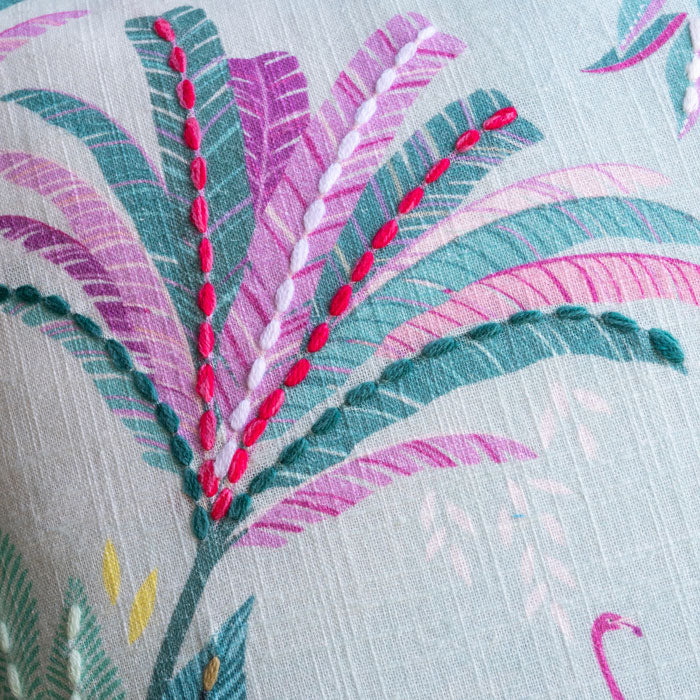 Close-up of embroidered fabric with pink and green palms on a light background