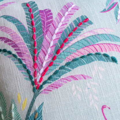 Close-up of embroidered fabric with pink and green palms on a light background