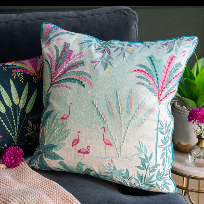 Decorative pillow in pinks and blues with flamingo and leaf pattern on a couch.