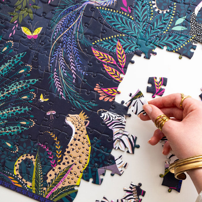 Colourful jungle themed puzzle with animals and foliage being completed, shows hand.