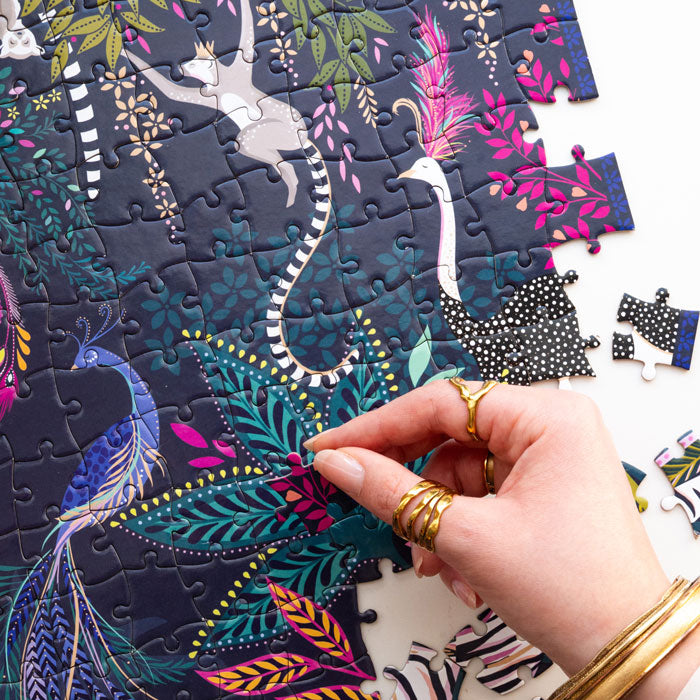 Colourful jungle themed puzzle with animals and foliage being completed, shows hand.