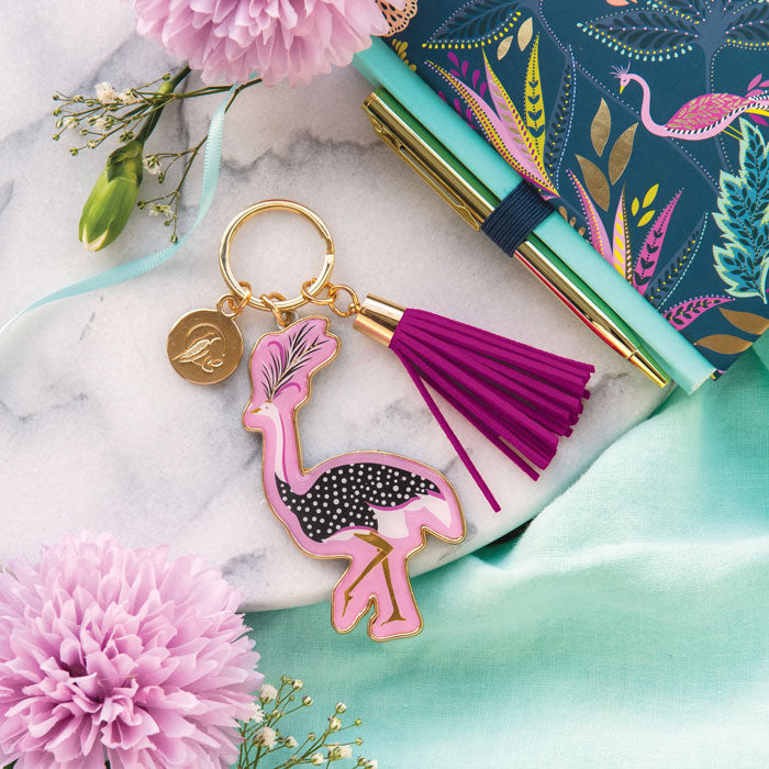 Flamingo keychain with tassel on a marble surface with flowers and a notebook.