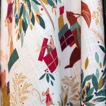 Close-up of tea towel with festive pattern featuring squirrels, presents, and foliage.