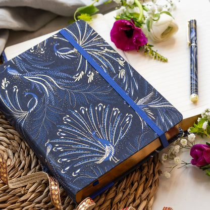 Notebook with peacock feather design on an indigo background with gold detailing, matching pen.
