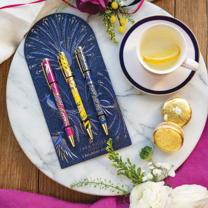 Set of three pens, one yellow, one cobalt and one fuchsia all in different floral designs on a decorative peacock design backing.