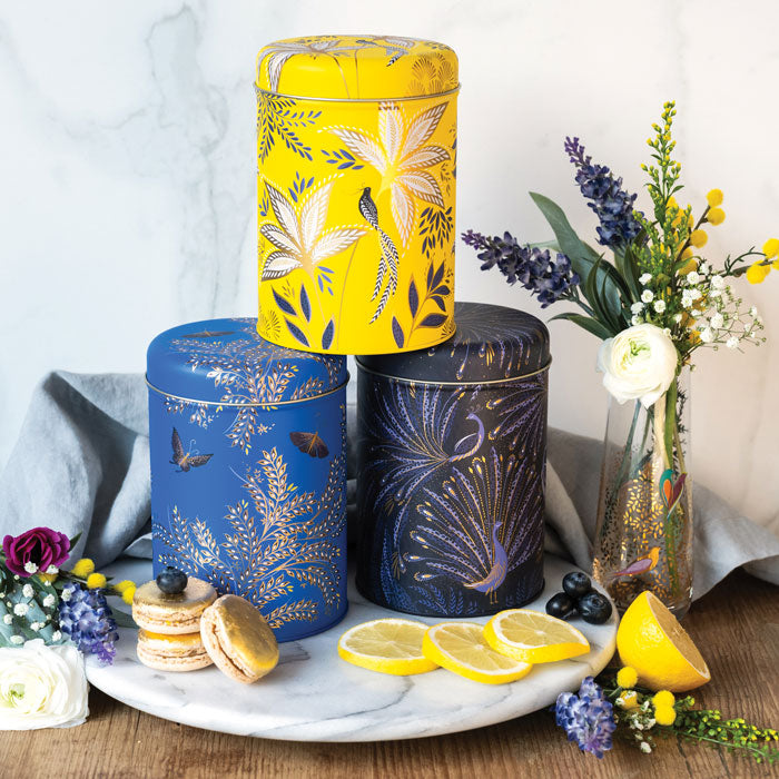 Three round tin storage caddies tacked, in different colours yellow, cobalt and indigo, each with different floral and bird designs.