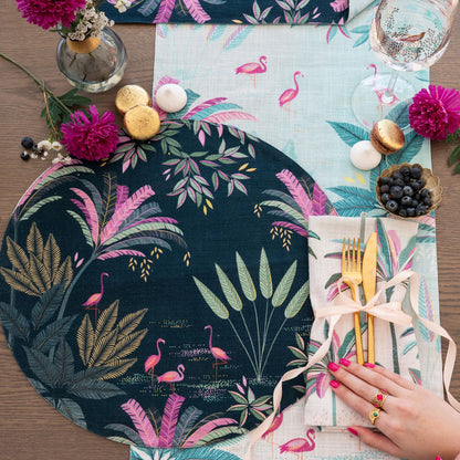 Decorative table setting with flamingo and leaf patterned placemats, gold cutlery, and colorful flowers.