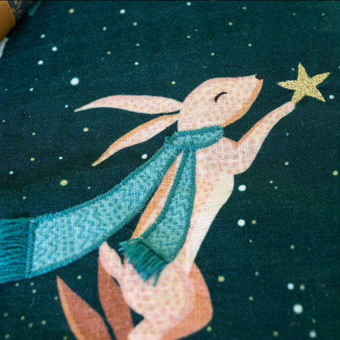Illustration of a rabbit holding a star against a dark green Christmas stocking.
