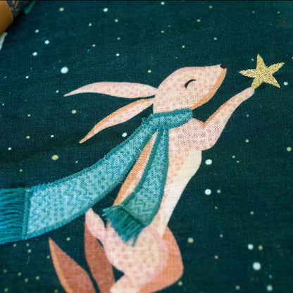 Illustration of a rabbit holding a star against a dark green Christmas stocking.