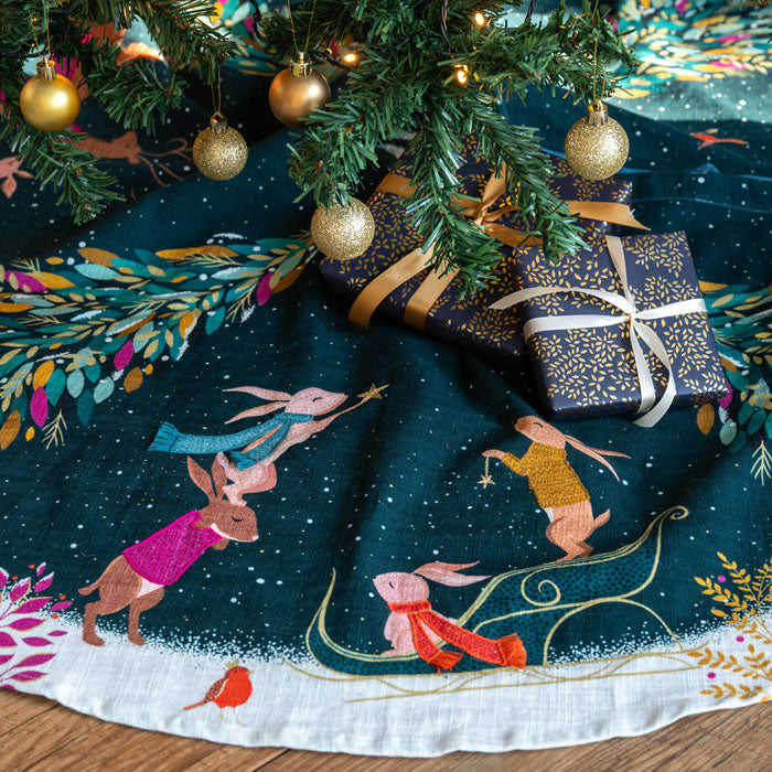 Decorative Christmas tree skirt with animated rabbits and presents underneath a tree.