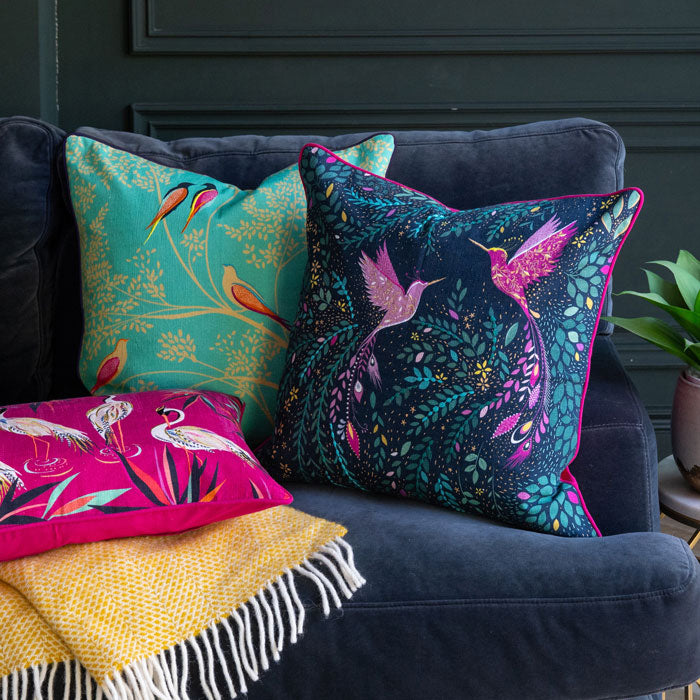 Blue cushion with pink hummingbirds and foliage design on the sofa with two other cushions.
