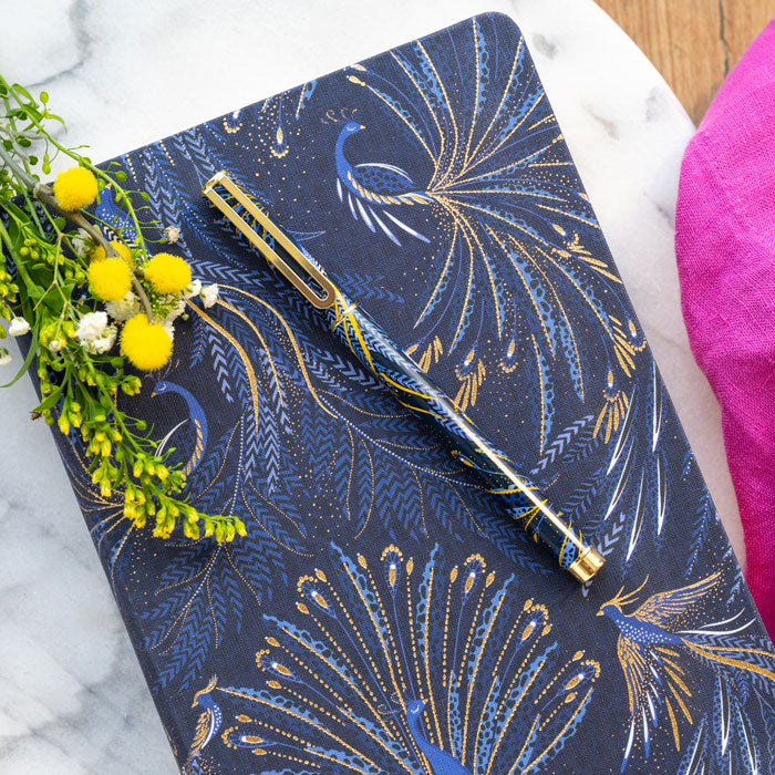 Notebook with peacock feather design on an indigo background with gold detailing, matching pen.