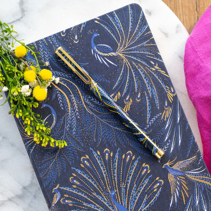 Notebook with peacock feather design on an indigo background with gold detailing, matching pen.