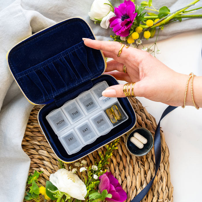 Hand holding the wellness organiser open, showing indigo velvet lining and plastic pill holder.