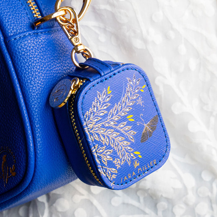 Cobalt earphones pouch with butterfly design and gold embellished details, shows gold clip attached to blue handbag.