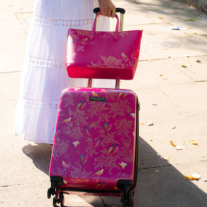 Person wheeling pink birds cabin case, with matching handbag.