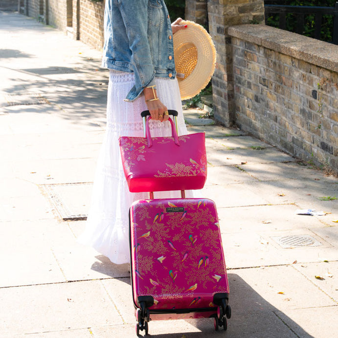 Person wheeling pink birds cabin case, with matching handbag.