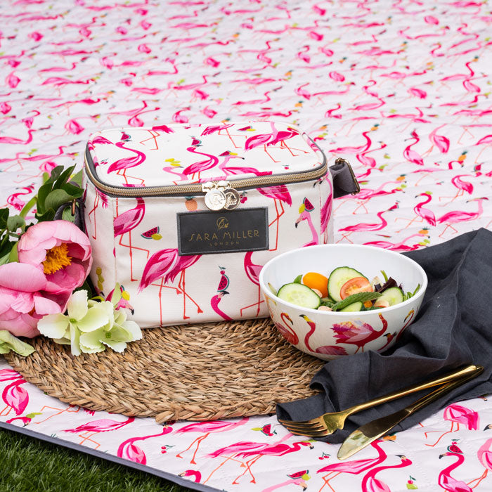 Cool bag with flamingo design on a matching blanket, accompanied by a bowl of salad and flowers.