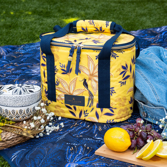 Yellow floral-patterned cooler bag on a picnic setup with lemons, grapes, and denim fabric.