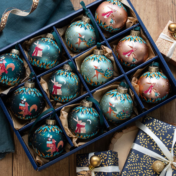 Decorative Christmas ornaments in a box with gift-wrapped presents on a wooden surface.