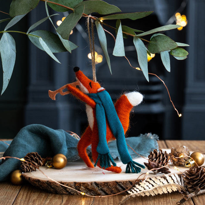 Decorative fox figurine wearing a blue scarf with Christmas decorations on a wooden surface.