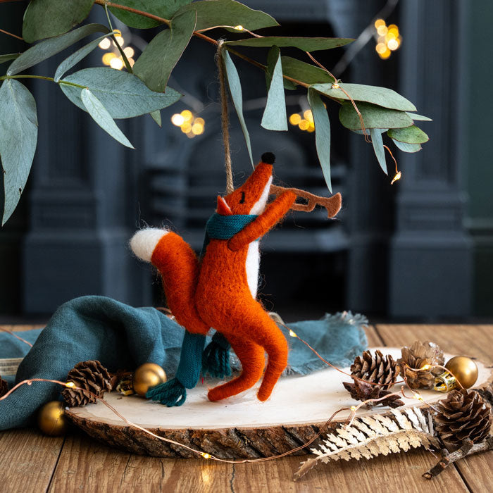 Decorative fox ornament on a wooden surface with greenery and lights in the background