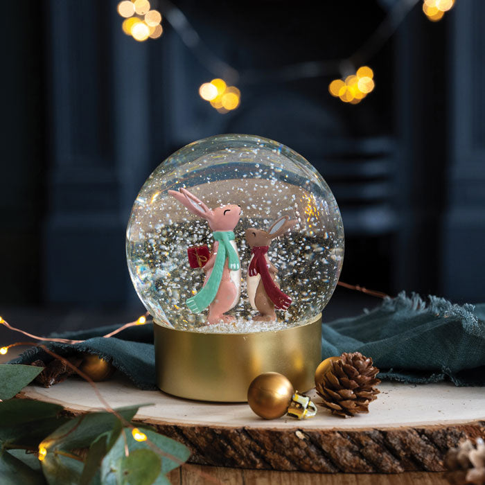 Decorative snow globe with two characters holding hands, sat on a wooden prop with lights in the background