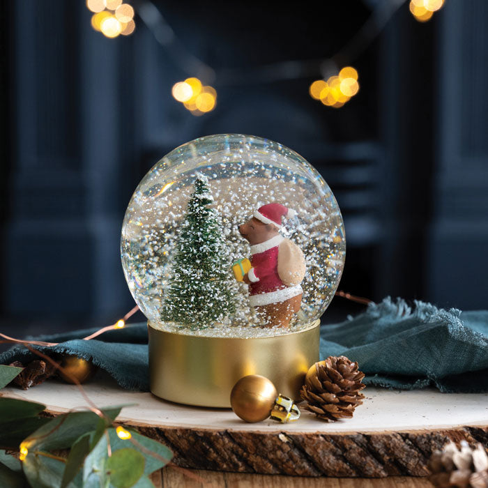 Christmas-themed snow globe with a bear and tree inside, surrounded by festive decorations.
