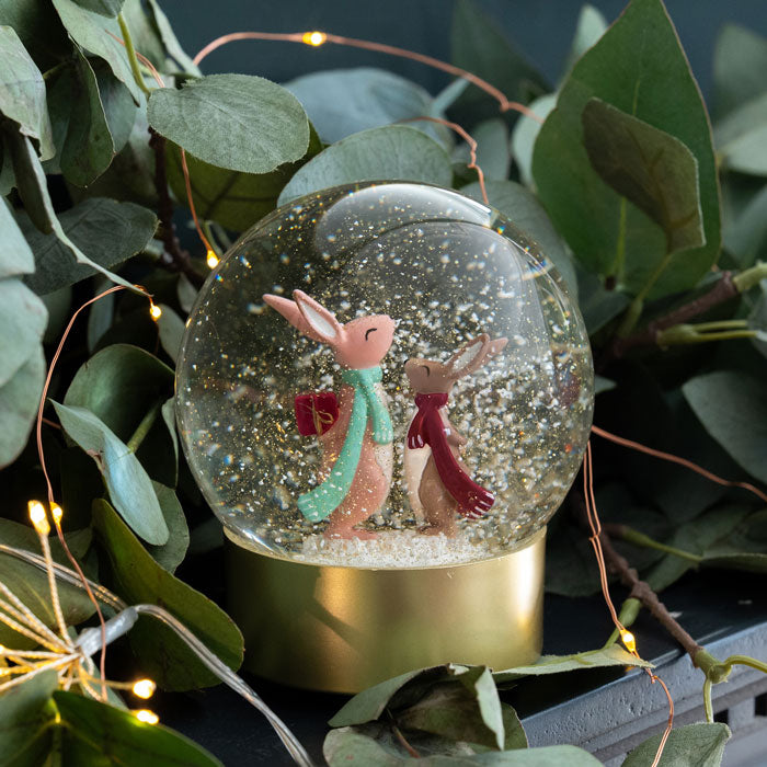 Snow globe with two rabbit characters surrounded by greenery and string lights