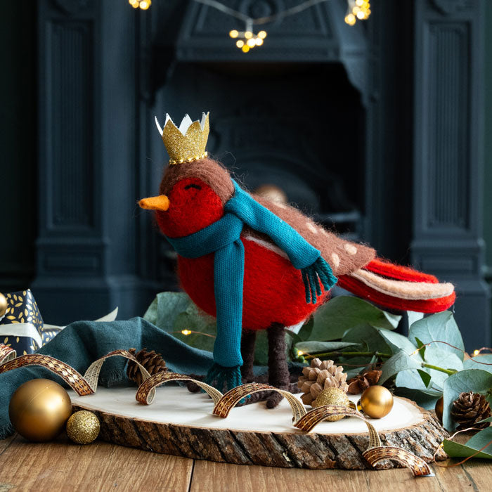 Decorative robin with a crown and scarf on a wooden surface with festive decorations.