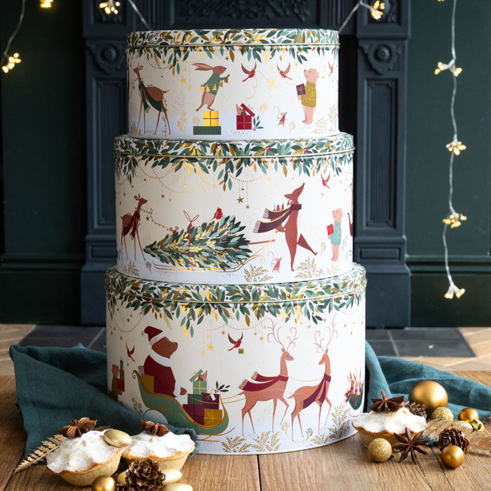 Stack of decorative Christmas-themed tins on a wooden surface with festive decorations.