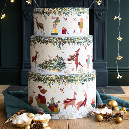 Stack of decorative Christmas-themed tins on a wooden surface with festive decorations.