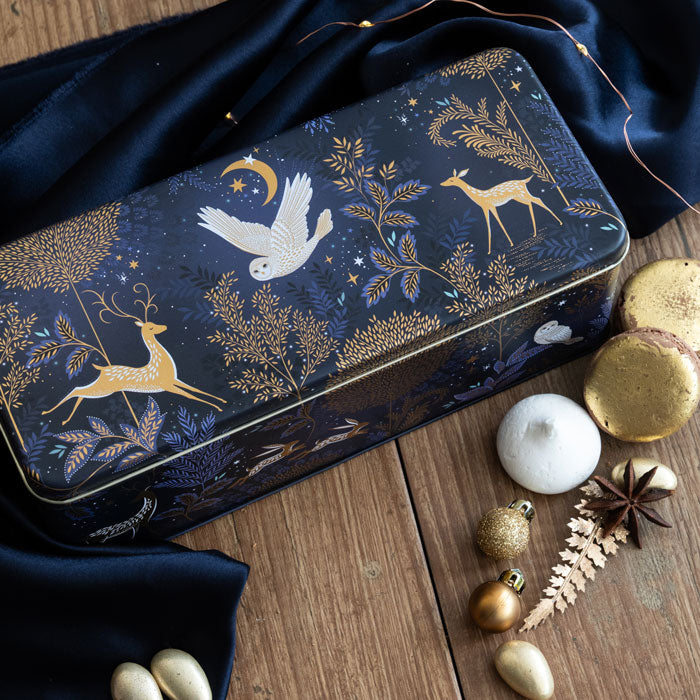 Decorative tin box with gold animal and nature patterns on a wooden surface with festive decorations.