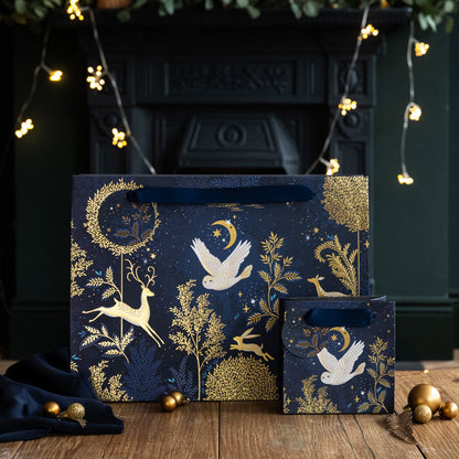 Decorative gift bags with gold animal and nature patterns on a wooden surface with a dark background.