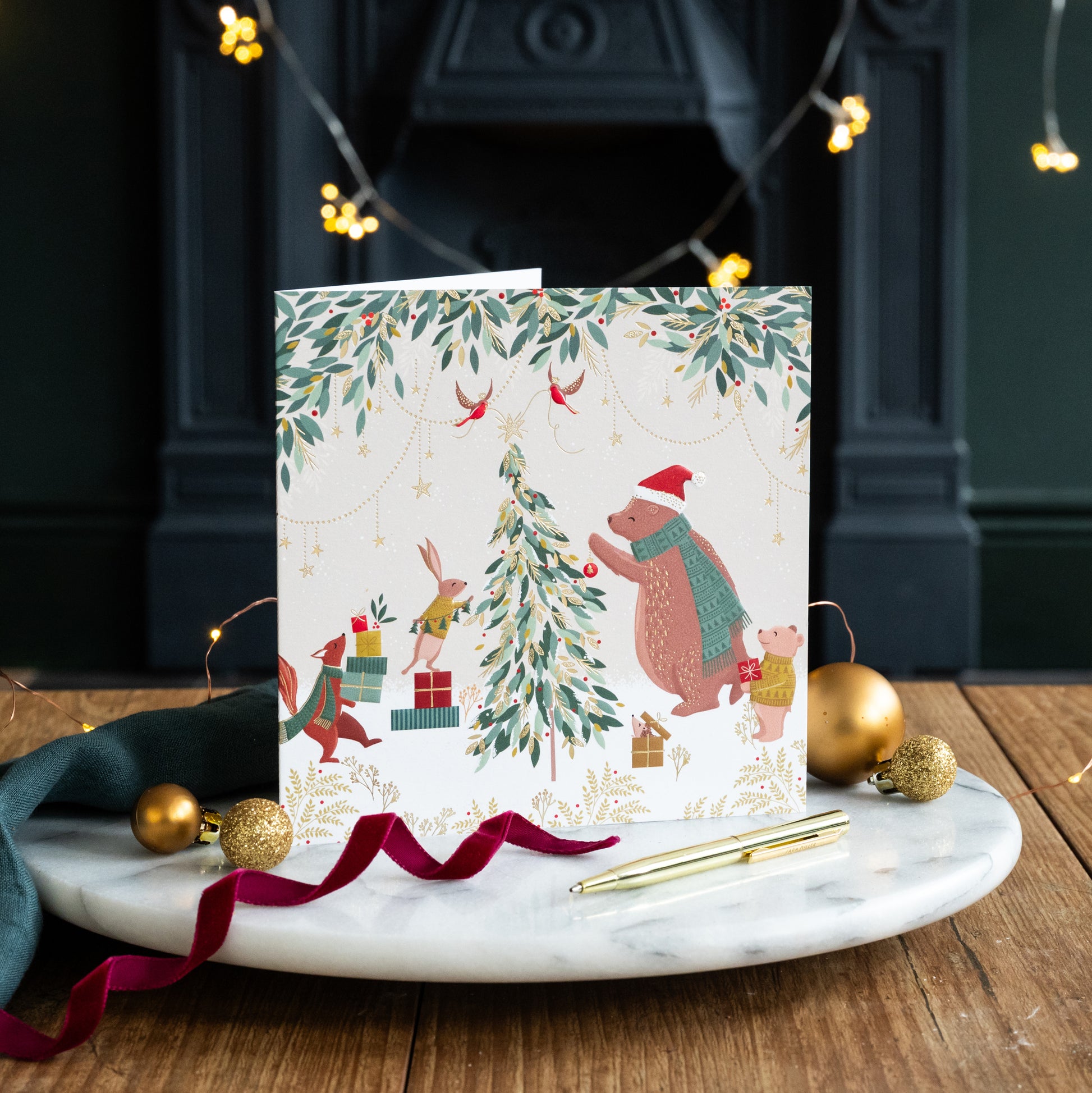 Christmas card with festive illustrations of animals around a tree on a marble surface with decorative items.