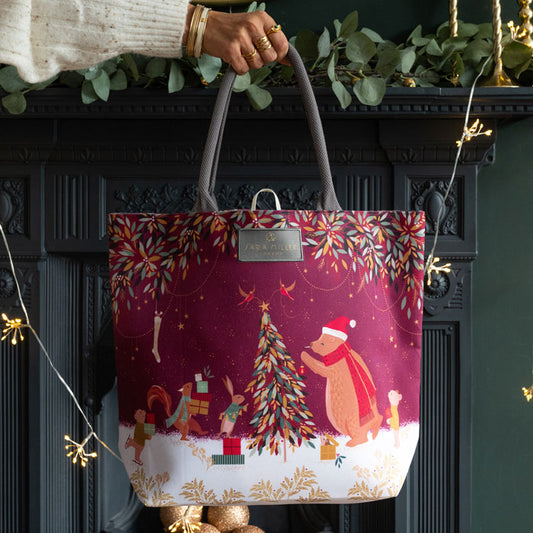 Christmas-themed tote bag held by a person in front of a decorated fireplace.