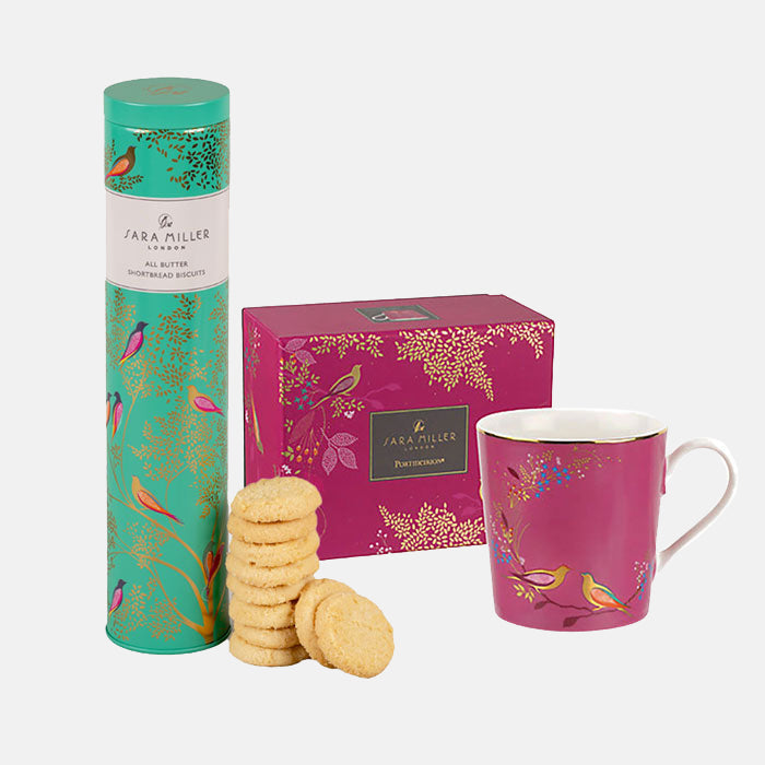 Pink mug with matching box next to a tin tube of shortbread with a green birds and branches design.